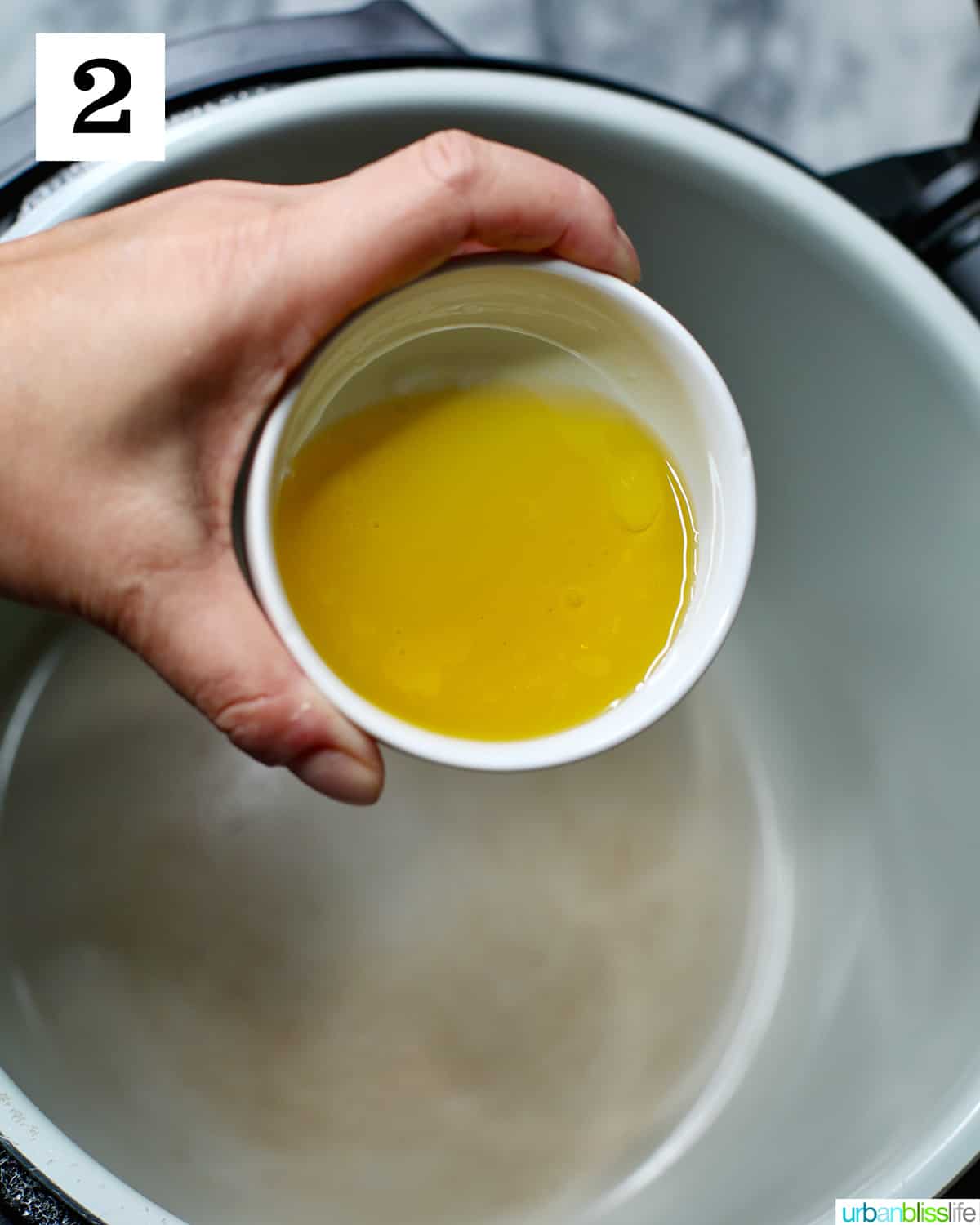 hand holding bowl of olive oil pouring into pot of a Ninja Foodi pressure cooker