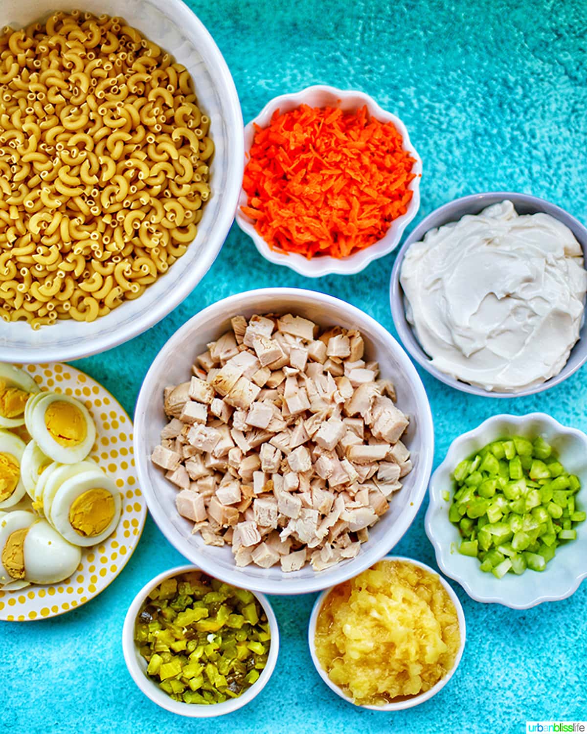 bowls full of ingredients to make Filipino Macaroni Salad on a bright blue background.