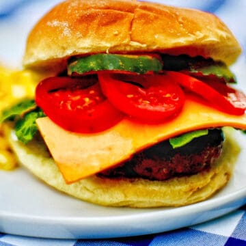 the ultimate burger with meat, cheese, tomatoes, pickls, bun, on a plate on checkered tablecloth