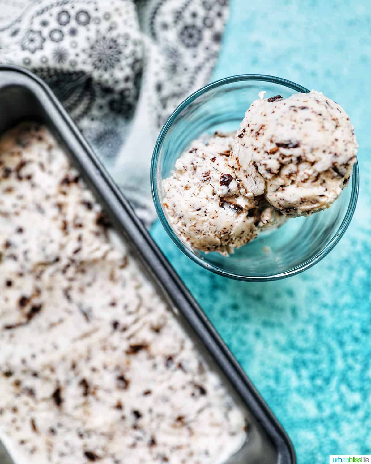 dairy-free chocolate chip ice cream in an ice cream scoop next to a pan of ice cream on a blue background.