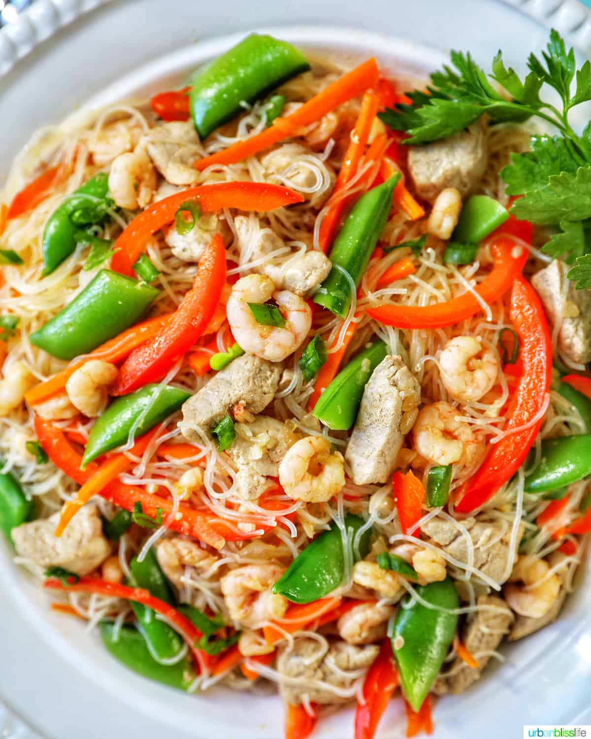 closeup of Filipino Pancit Bihon - noodles, shrimp, chicken, snap peas, red peppers- in a bowl.