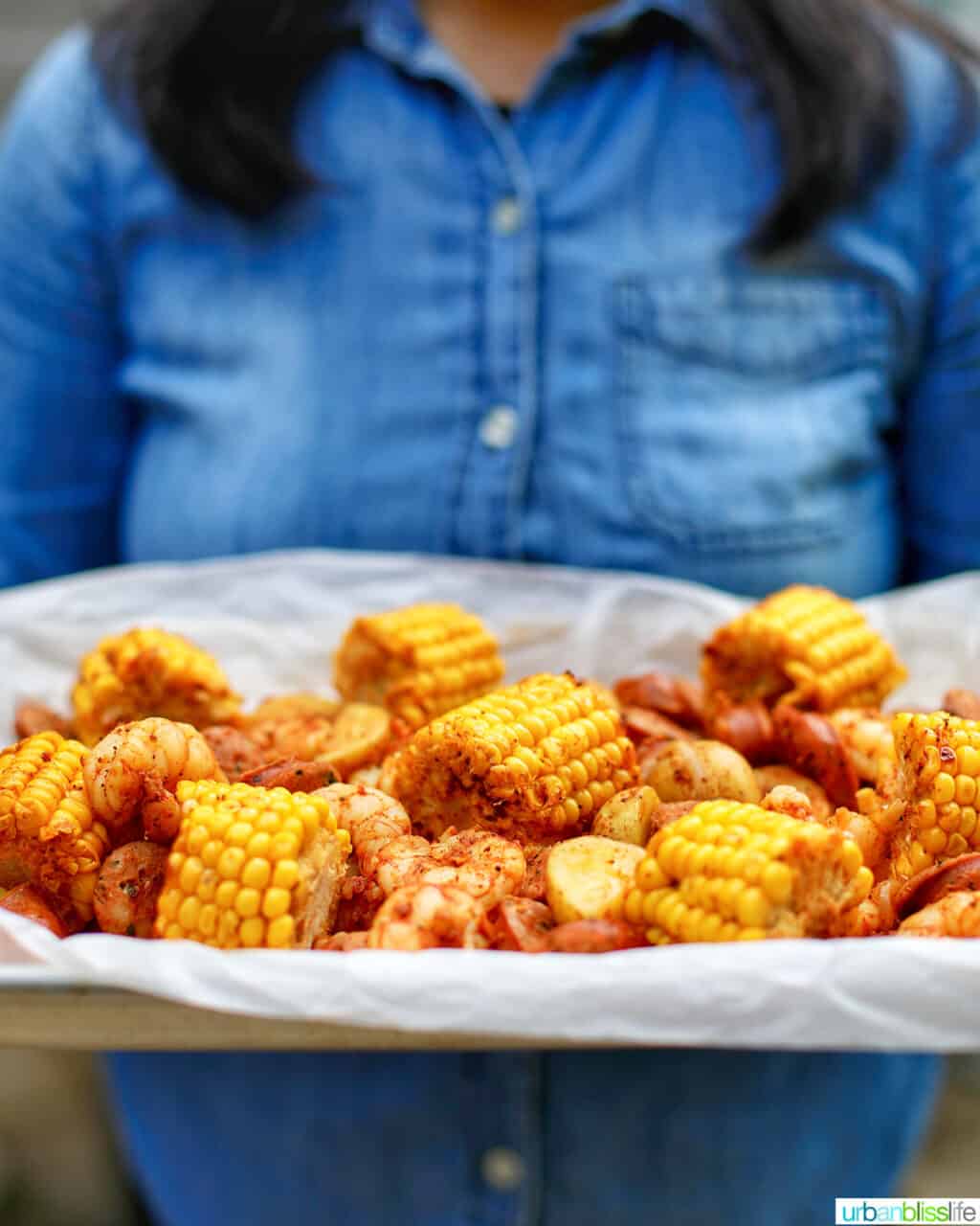 holding a tray of low country seafood boil foil packets against denim shirt