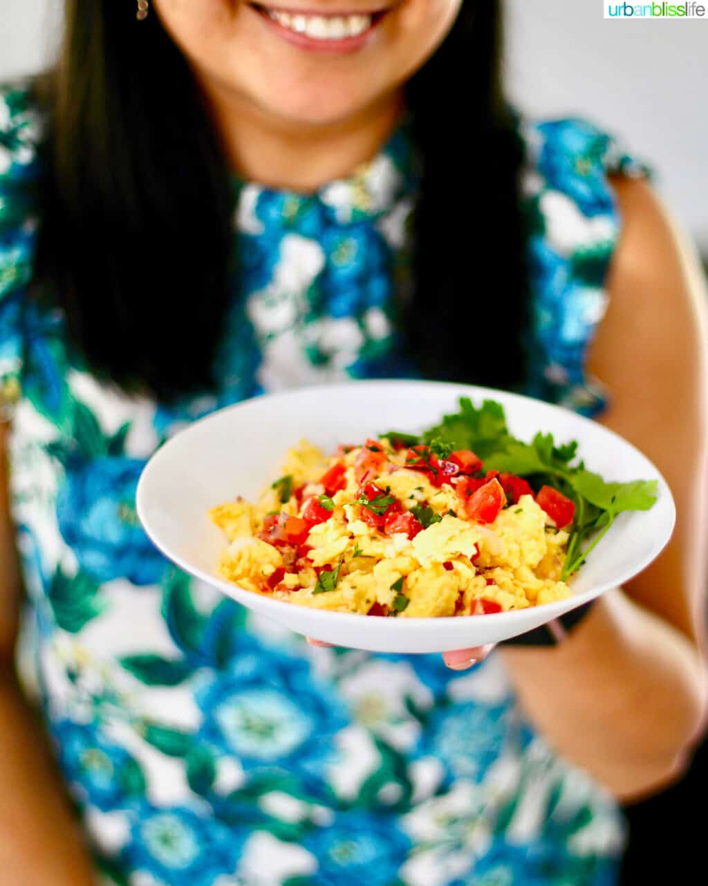 holding bowl of salsa eggs against backdrop of blue and white floral shirt