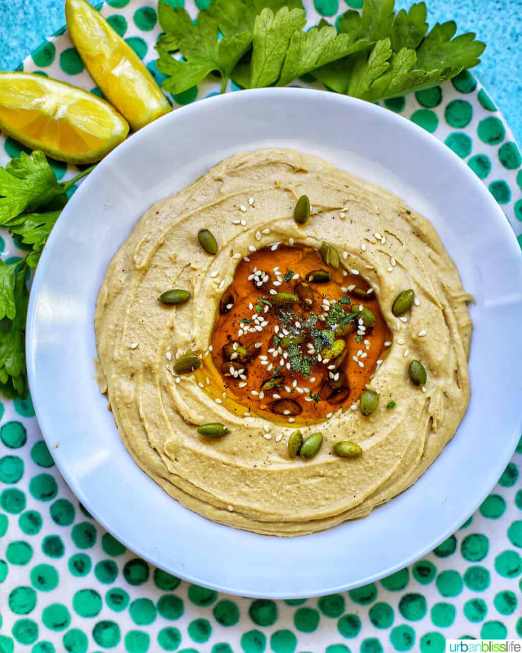 hummus in a white bowl on green polka dot platter with lemon slices