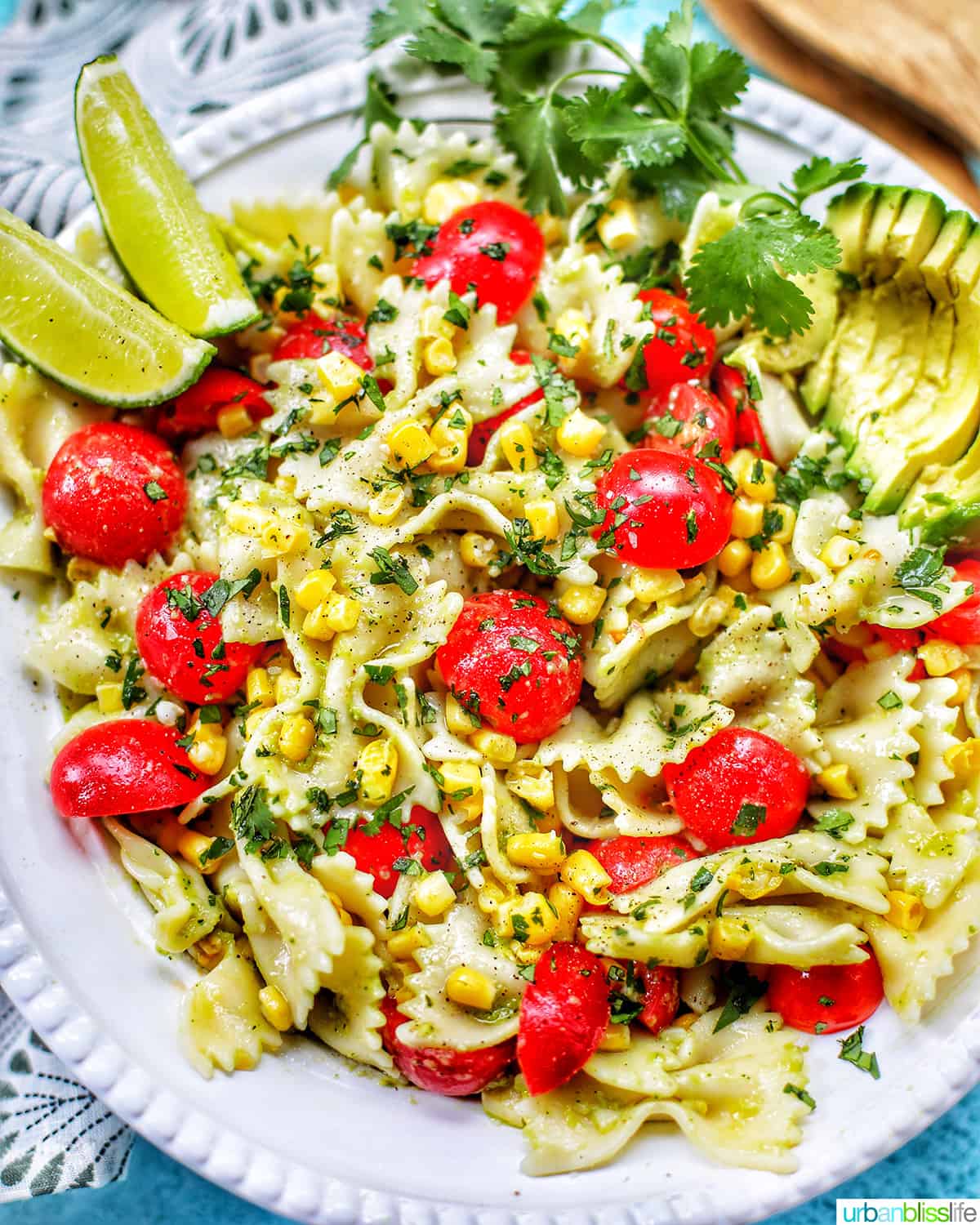 avocado salad with tomatoes and corn in a big white bowl with lime wedges.