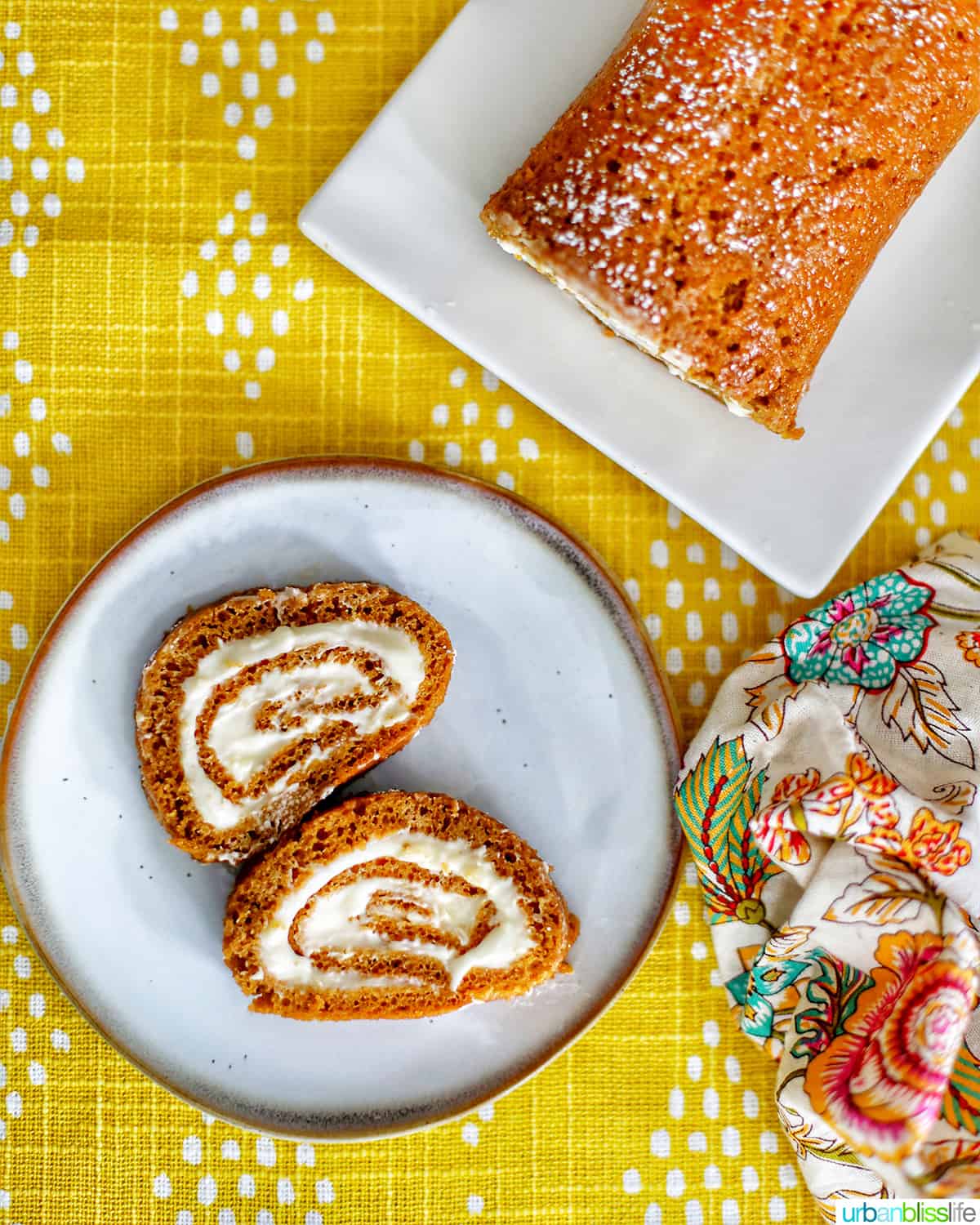 pumpkin cream cheese roll up and slices on plates and yellow tablecloth with colorful napkin.