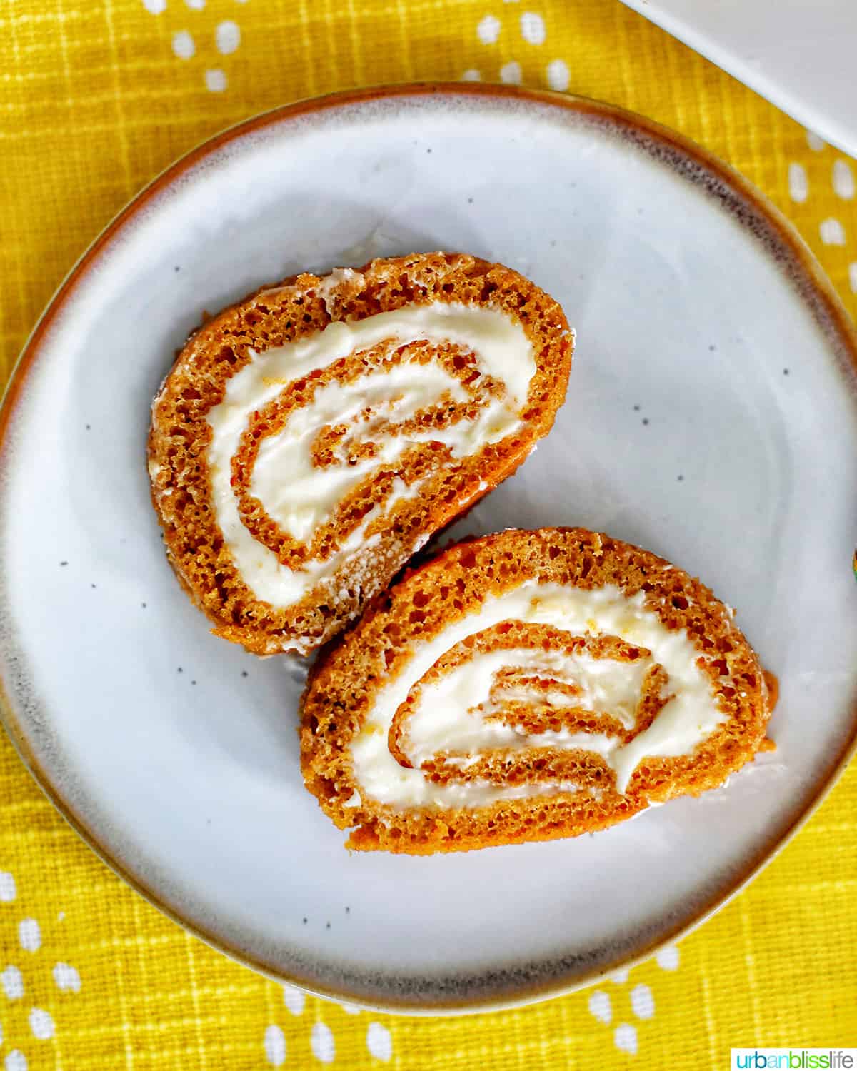 pumpkin cream cheese roll on a plate and yellow tablecloth.