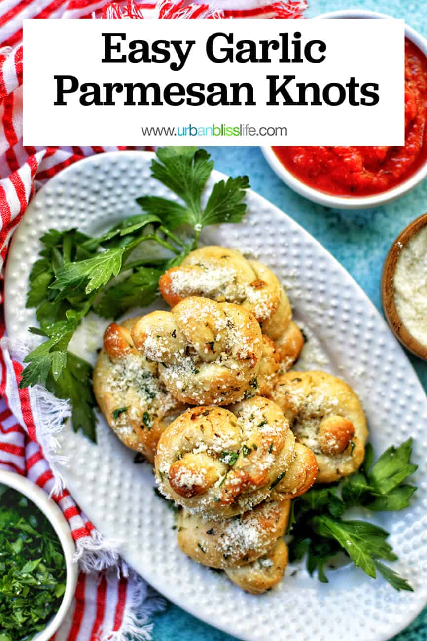 garlic parmesan knots on a white platter with sides of dipping sauce, cheese, parsley