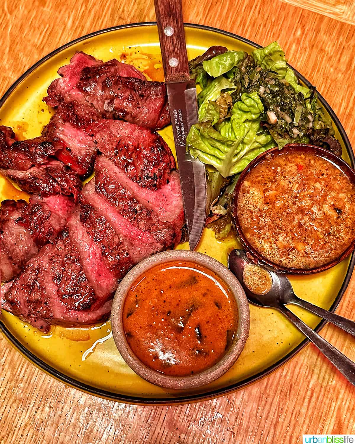 plate of sliced rib eye steak and sauces on a wood table at Phuket Cafe.