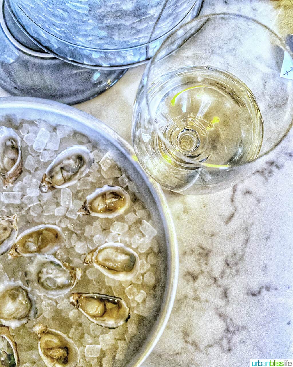 glass of white wine next to a round tray of oysters on ice at normandie restaurant in Portland, Oregon.