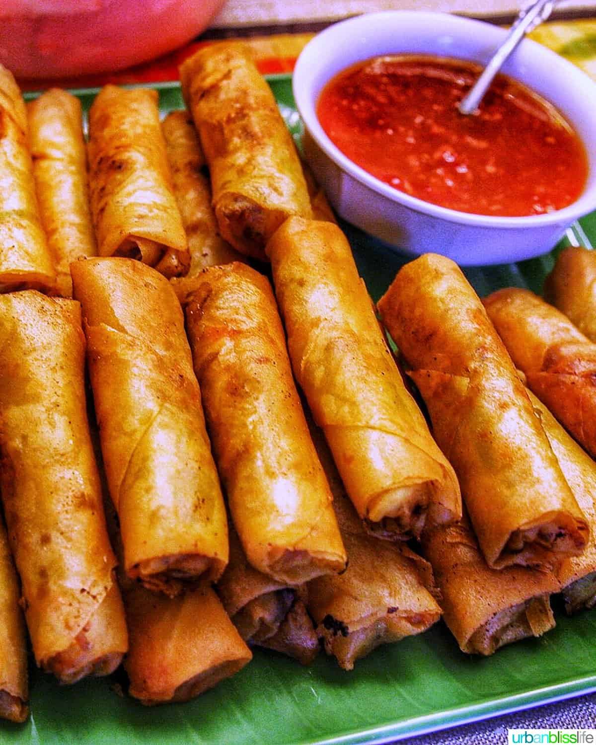 Tray of Filipino lumpia egg rolls stacked with dipping sauce in a bowl.