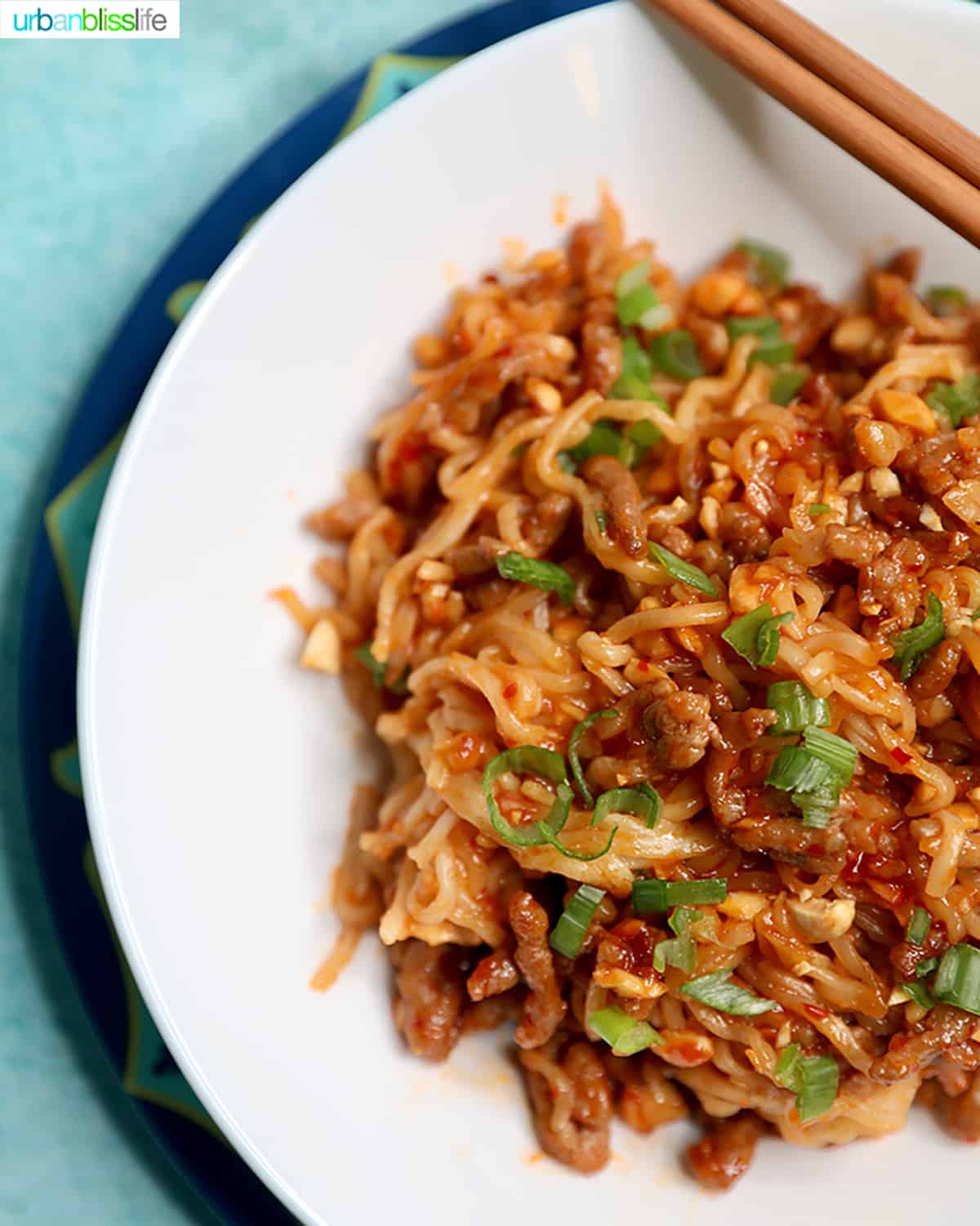 pork and peanut dragon noodles with green onions on a white plate with chopsticks.