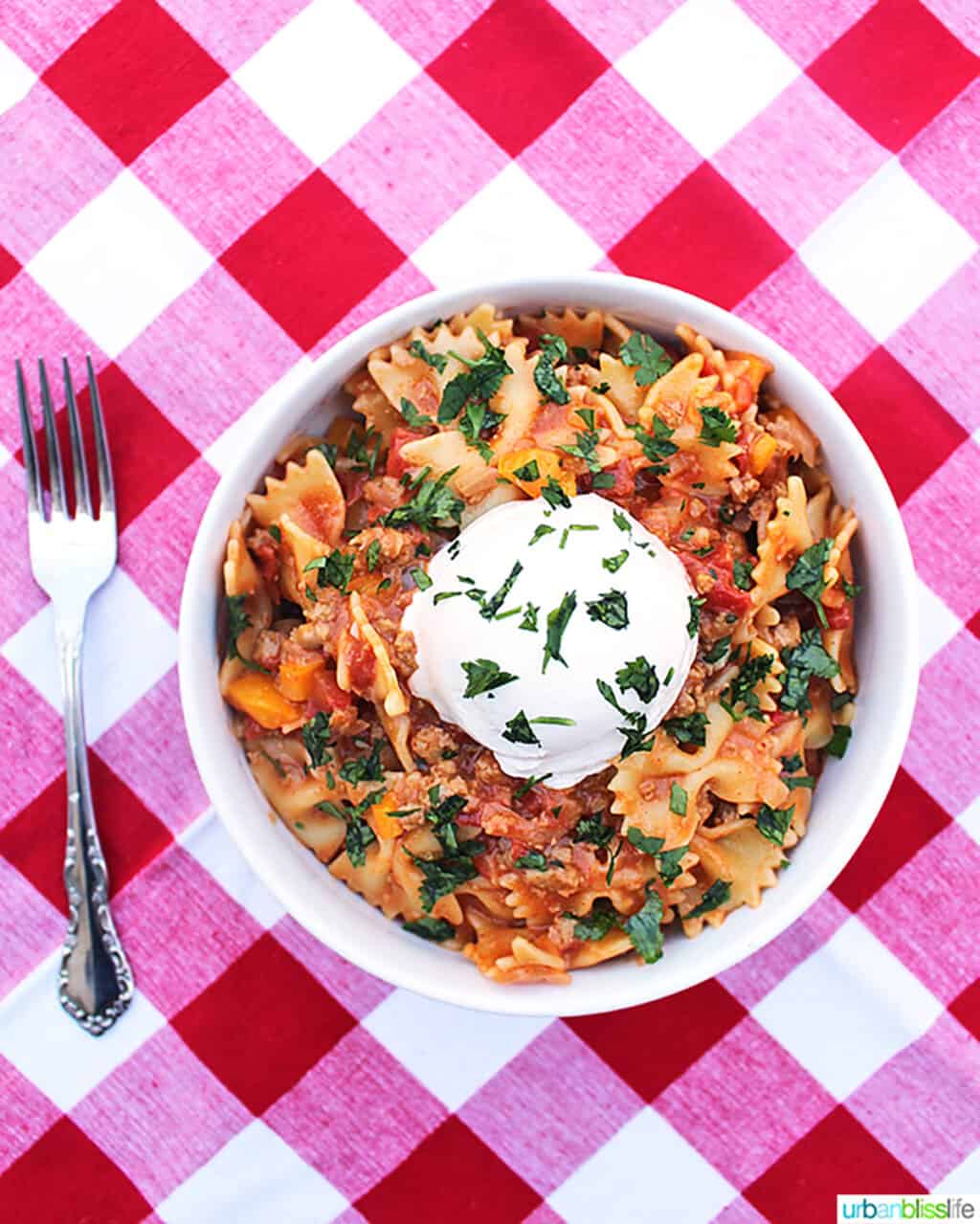 white bowl of Taco Pasta on red and white checkered tablecloth with fork