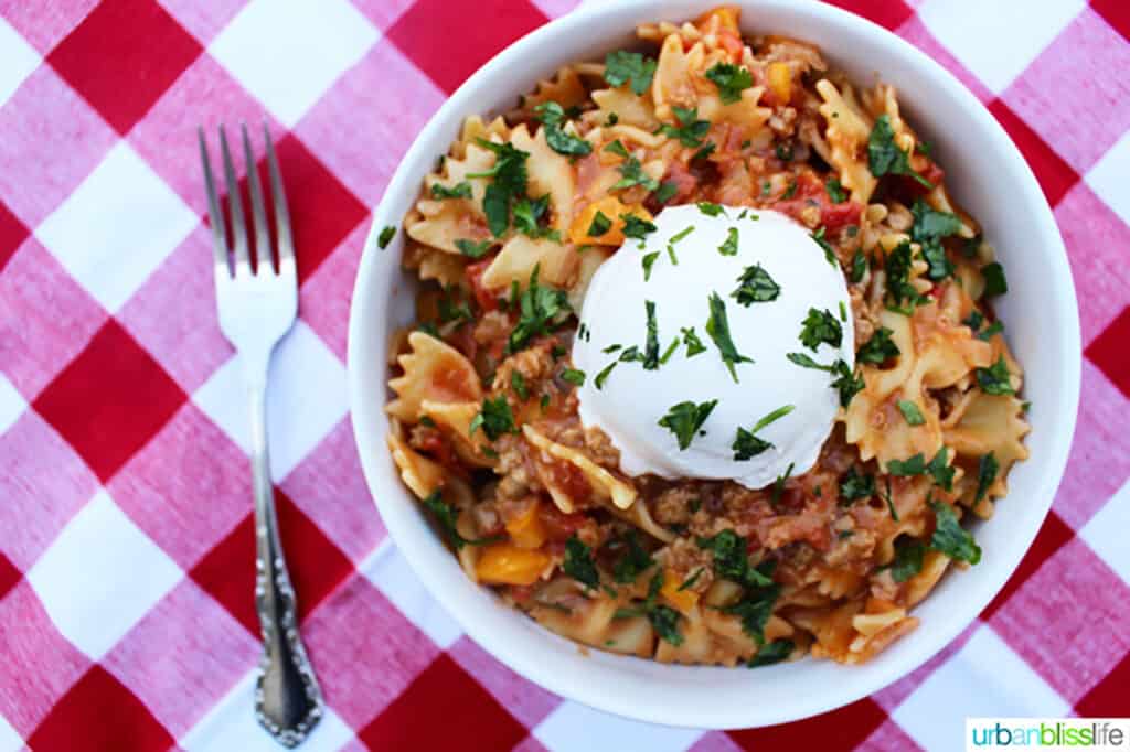 white bowl of Taco Pasta on red and white checkered tablecloth with fork