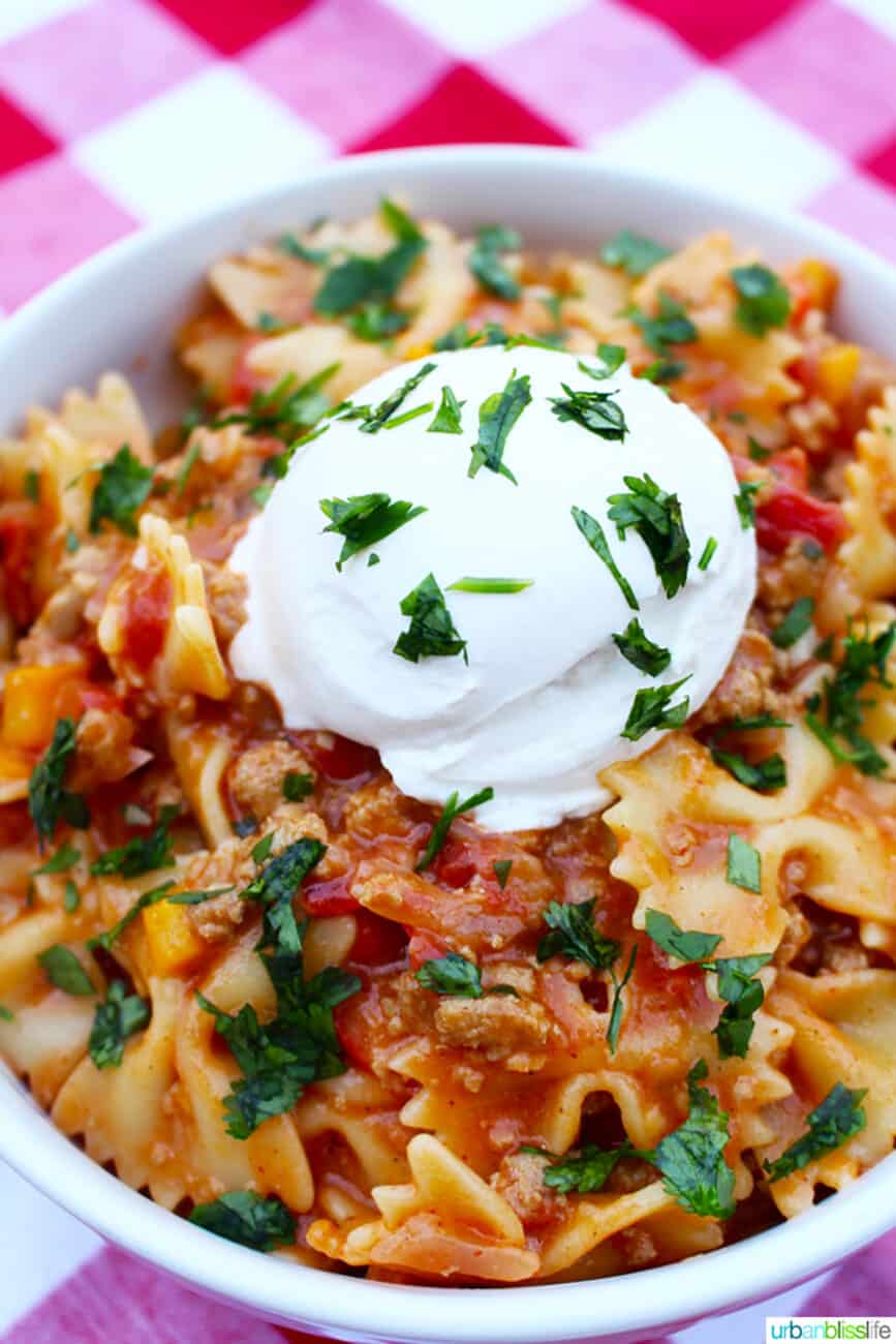 white bowl of Taco Pasta on red and white checkered tablecloth with fork