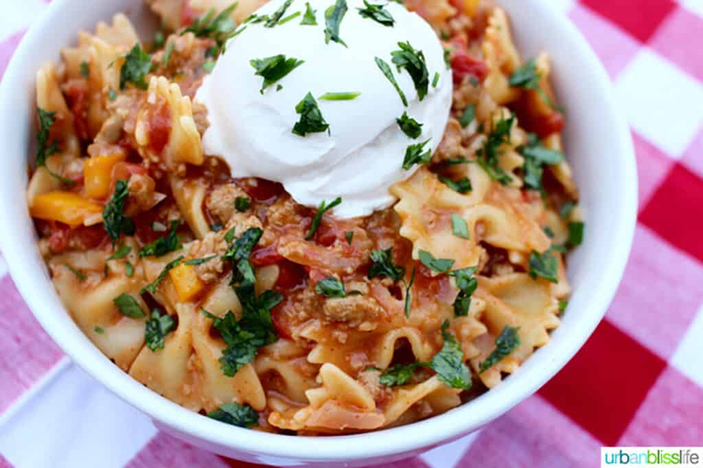 white bowl of Taco Pasta on red and white checkered tablecloth with fork