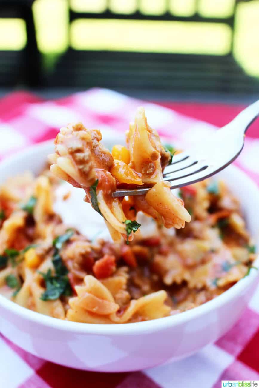 white bowl of Taco Pasta on red and white checkered tablecloth with fork