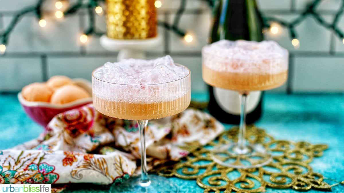 two glasses of champagne sherbet floats with twinkling lights and Champagne bottle in background and colorful decor.