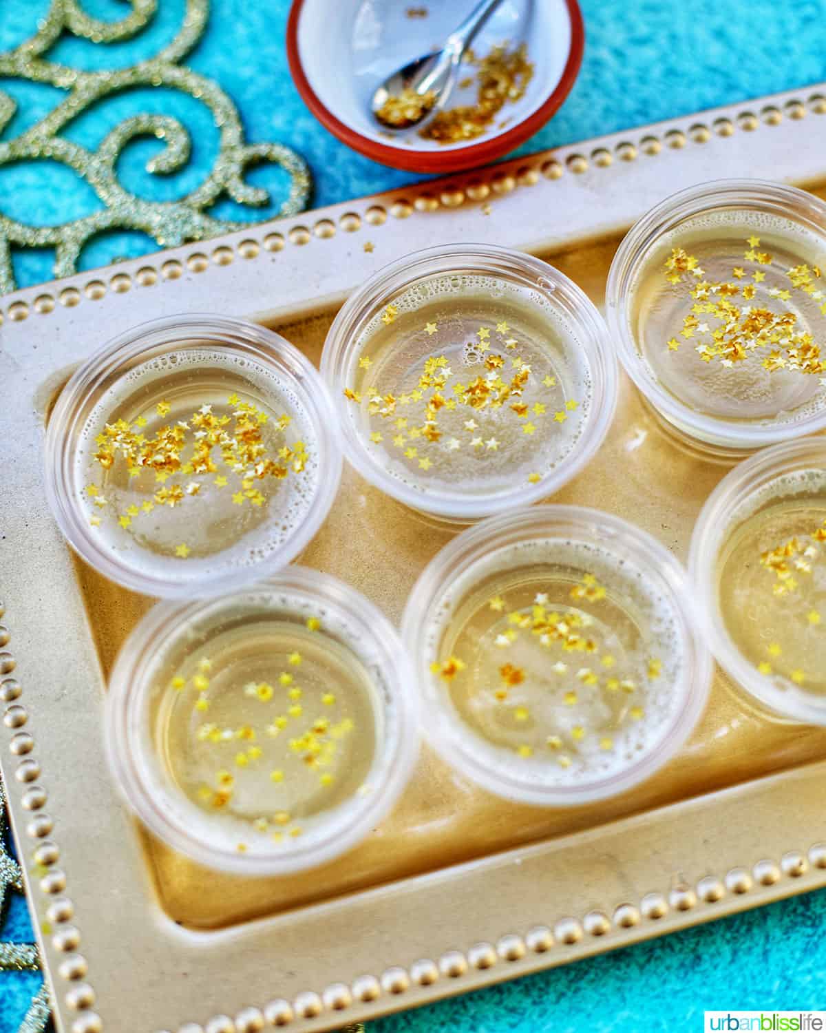 two rows of Champagne Jello Shots on a gold serving platter on blue background.