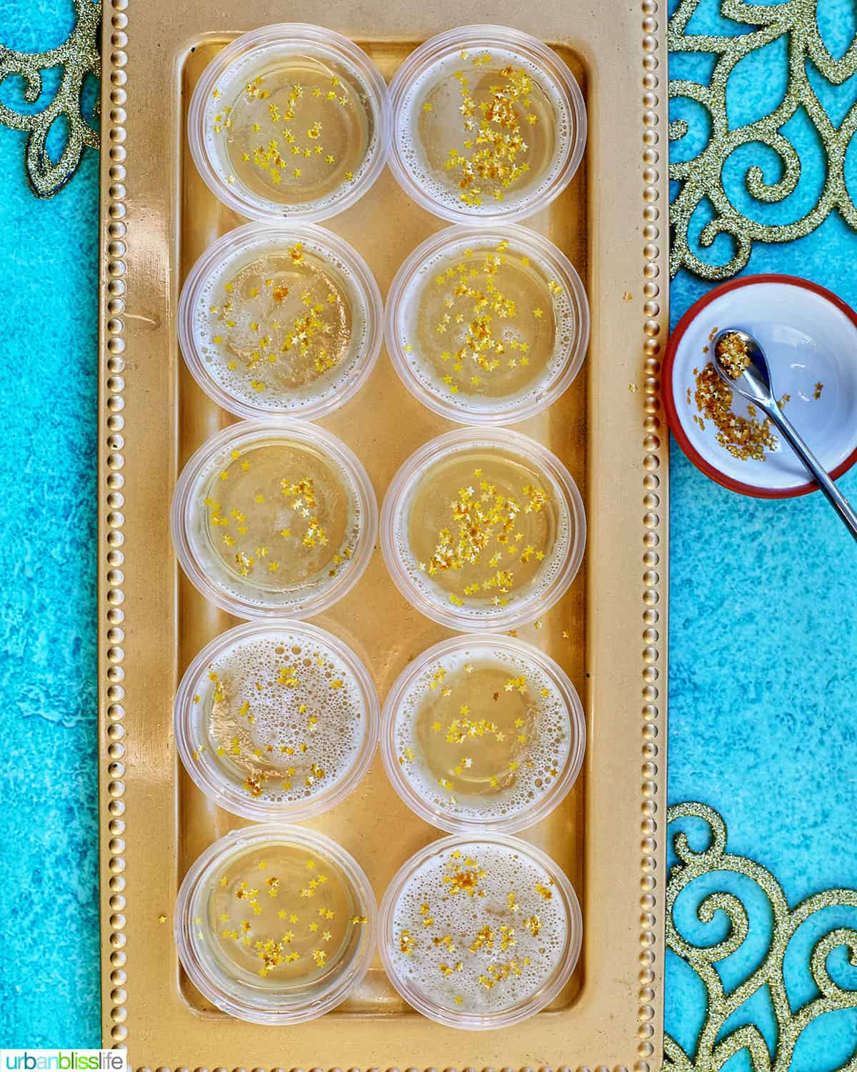 two rows of Champagne Jello Shots on a gold serving platter on blue background.
