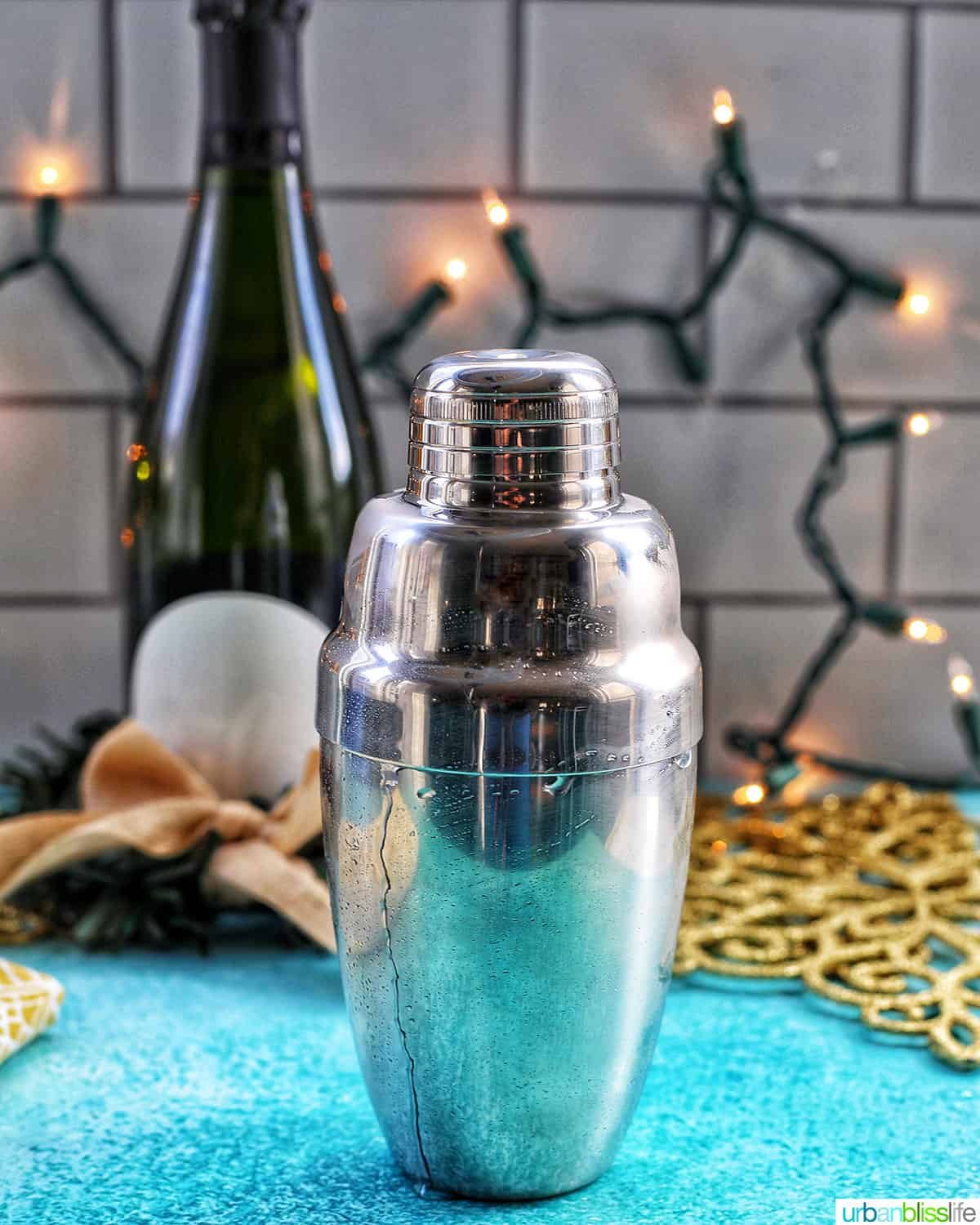 cocktail shaker with champagne and twinkly lights in background and blue table.