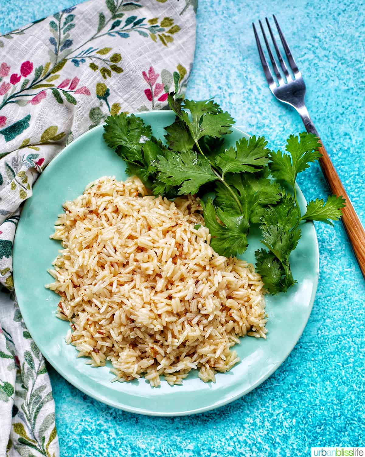 plate of instant pot garlic rice with herbs, a fork, colorful napkin, on a bright blue table.