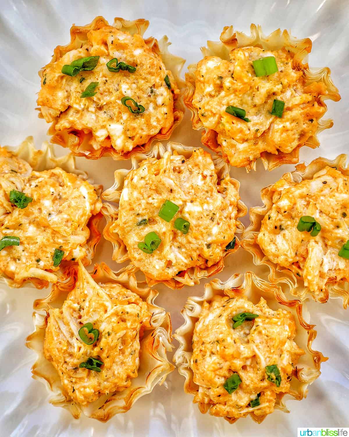 several buffalo chicken bites with chopped green onions on a plate.