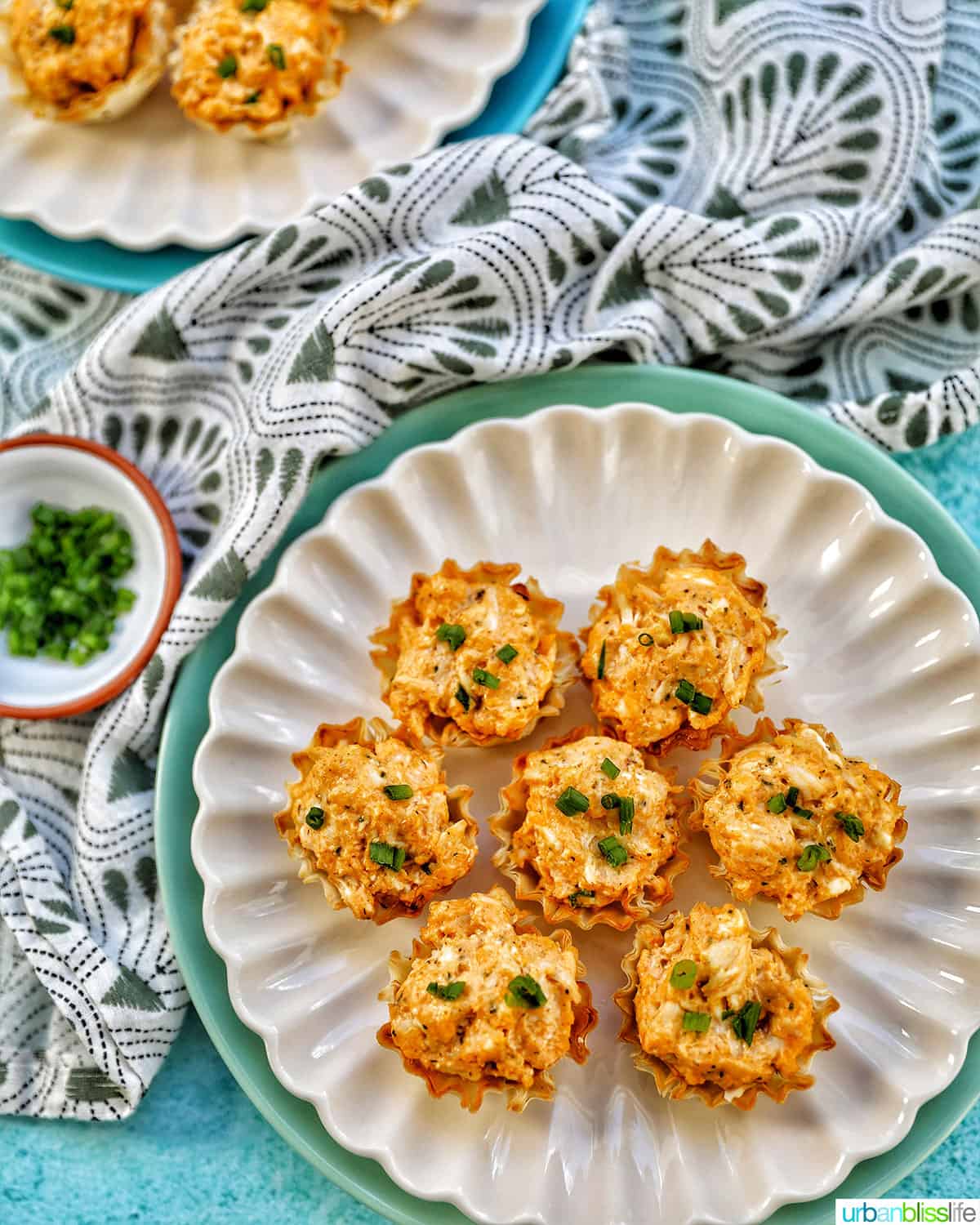 several buffalo chicken bites with chopped green onions on plates with a green and white napkin.