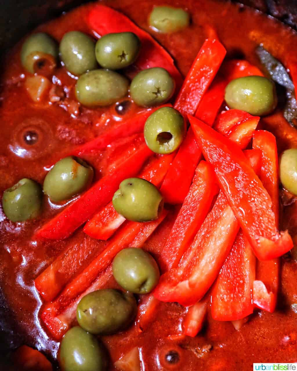 adding red peppers and green olives to pot of beef caldereta