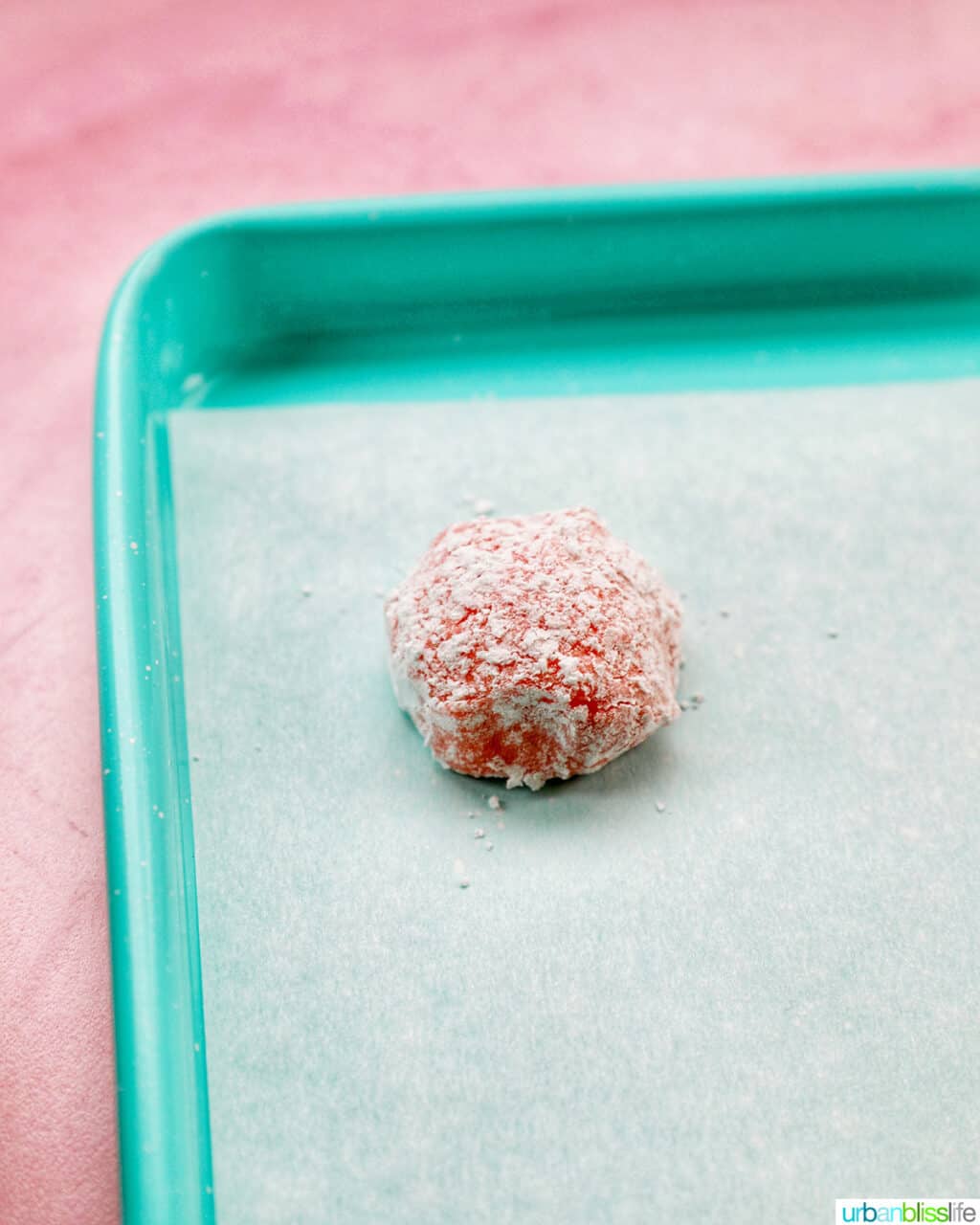 strawberry crinkle cookie dough ball rolled in powdered sugar on baking sheet