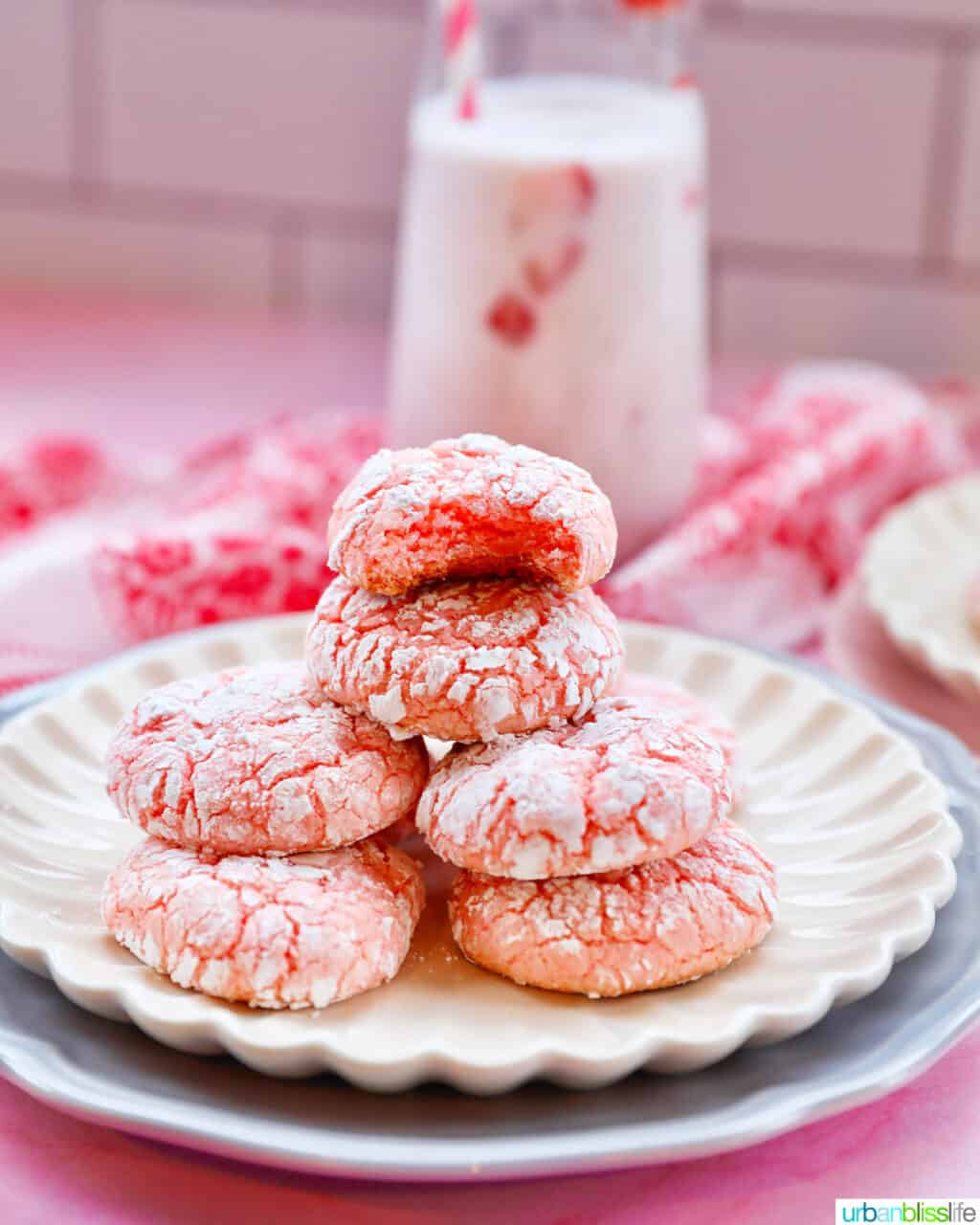stack of strawberry crinkle cookies on a plate with strawberry milk in the background