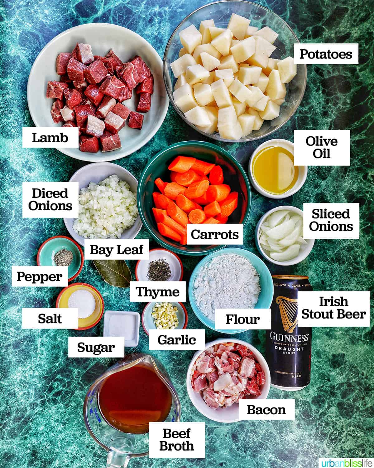 ingredients in several individual bowls to make Irish lamb stew on a marbled green background.