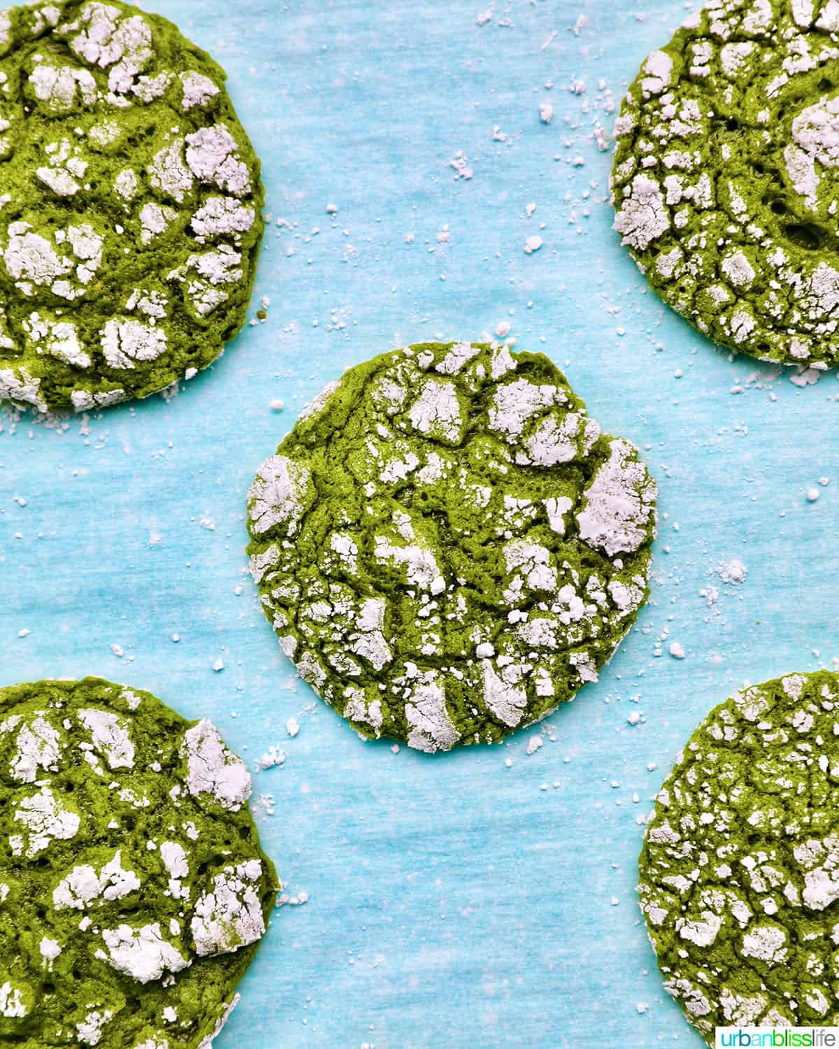 closeup tray of bright green matcha crinkle cookies with powdered sugar sprinkles.