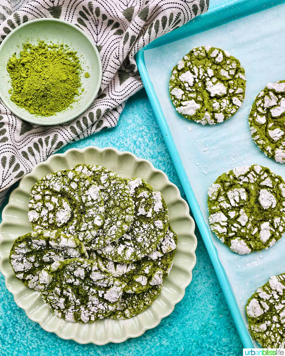 plate of bright green matcha crinkle cookies stacked on top of one another on a bright blue background.