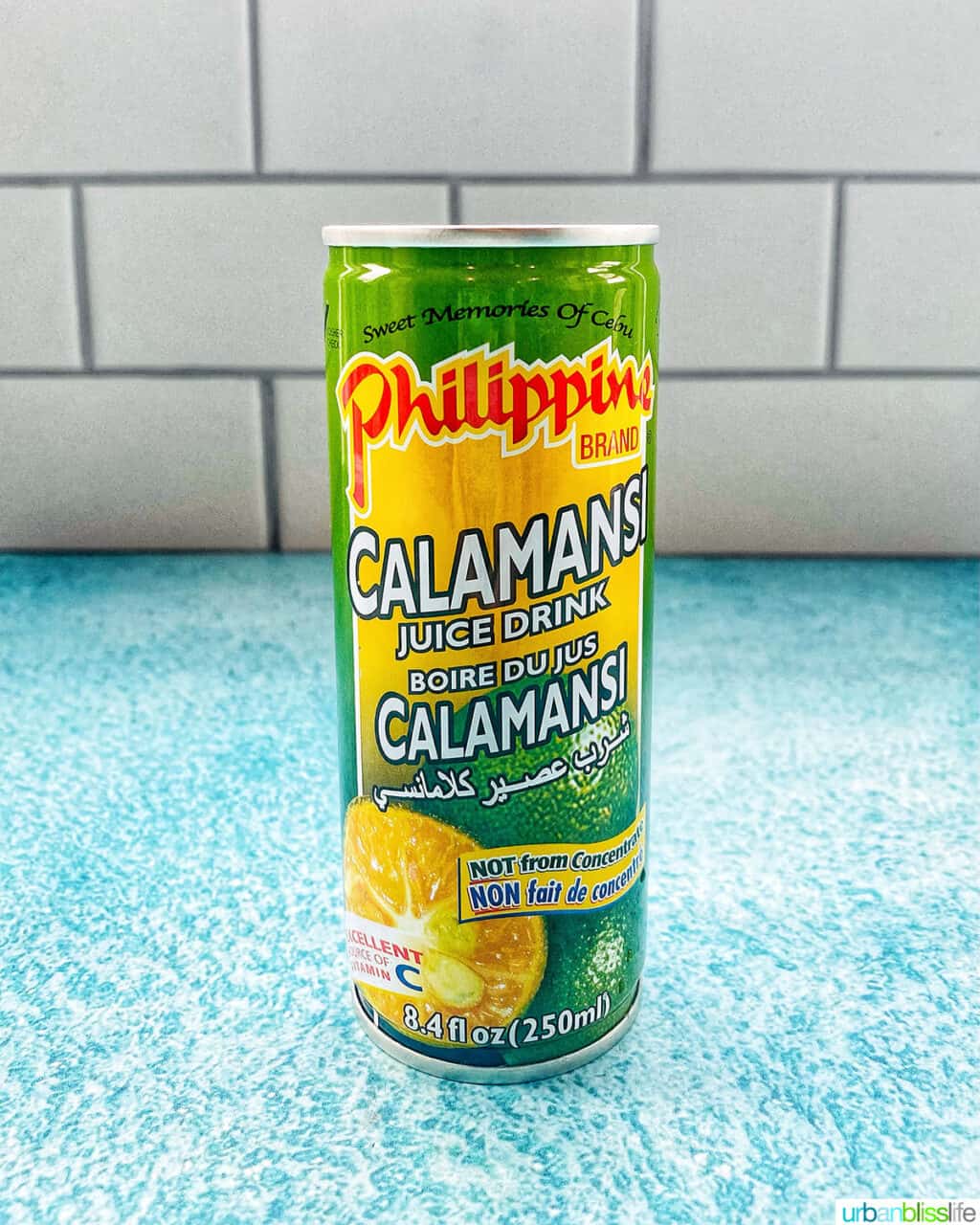 green and yellow can of calamansi juice on a bright blue table with kitchen tile background.