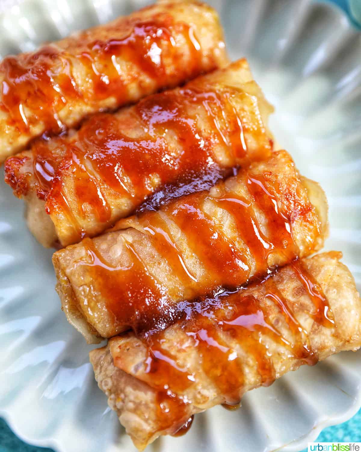 four turon (Filipino banana lumpia) on a scalloped plate drizzled with caramel sauce.