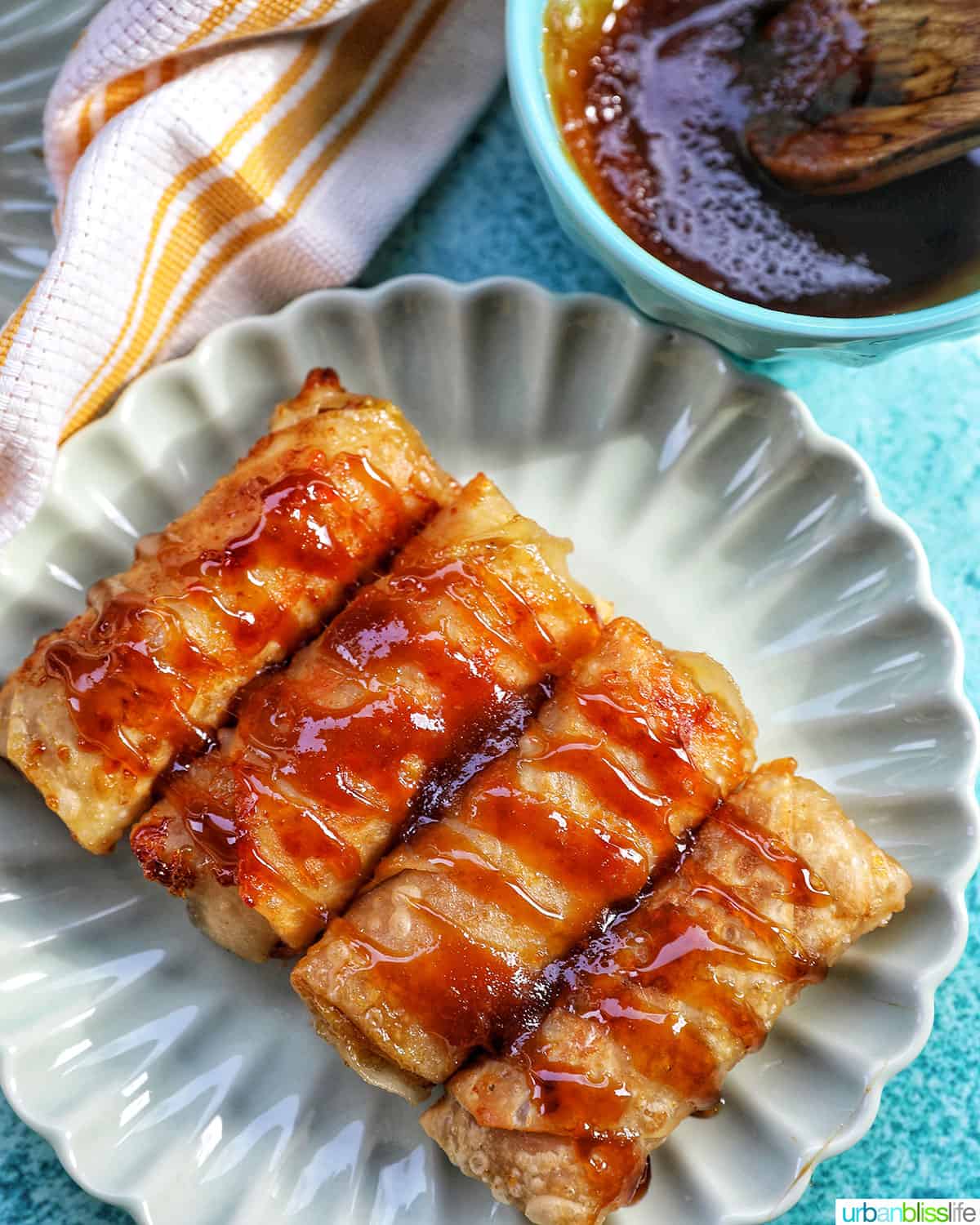 plate of four turon Filipino banana lumpia with drizzled caramel sauce on a blue background.