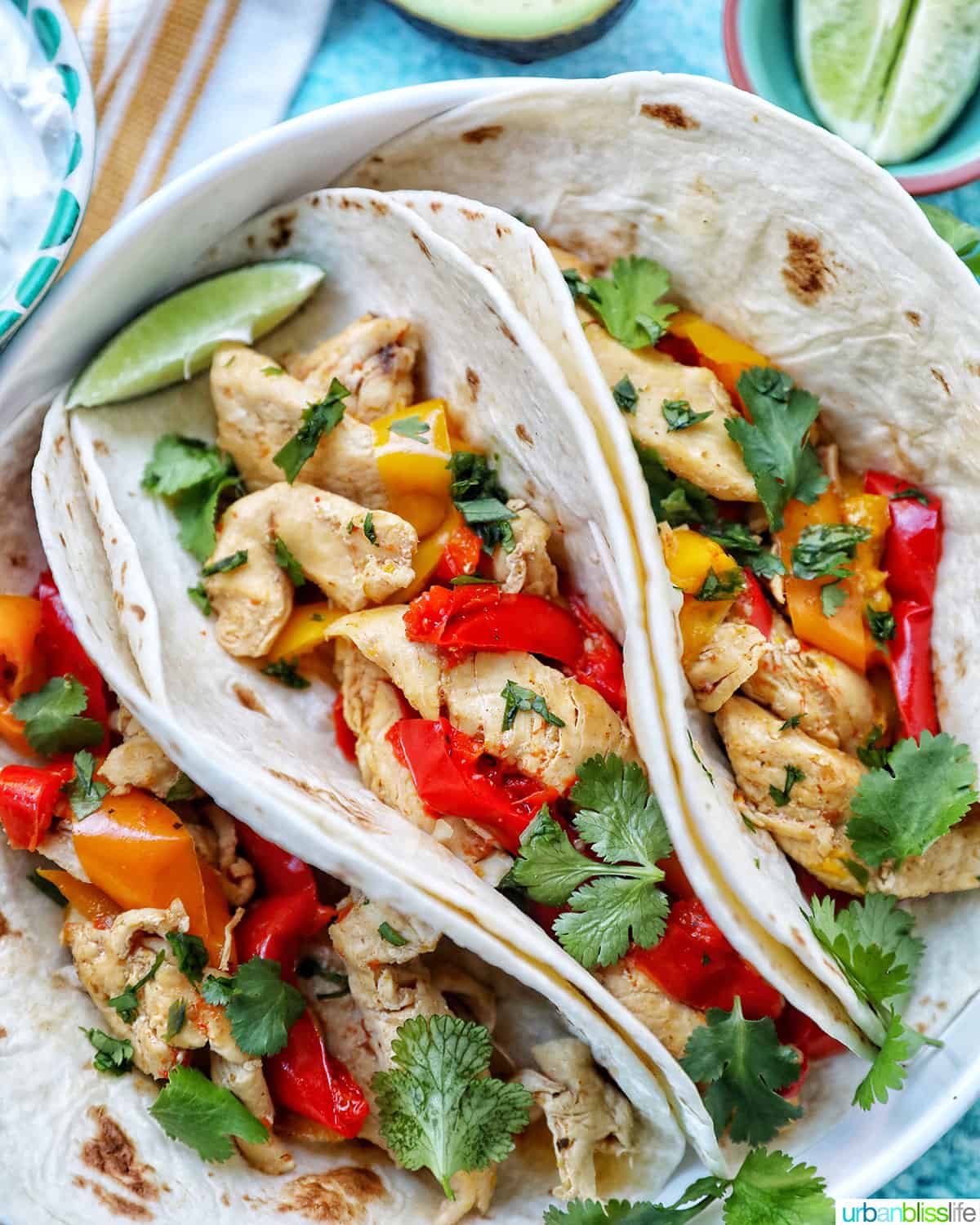 three instant pot chicken fajitas with red and yellow peppers, lime wedges, and cilantro.