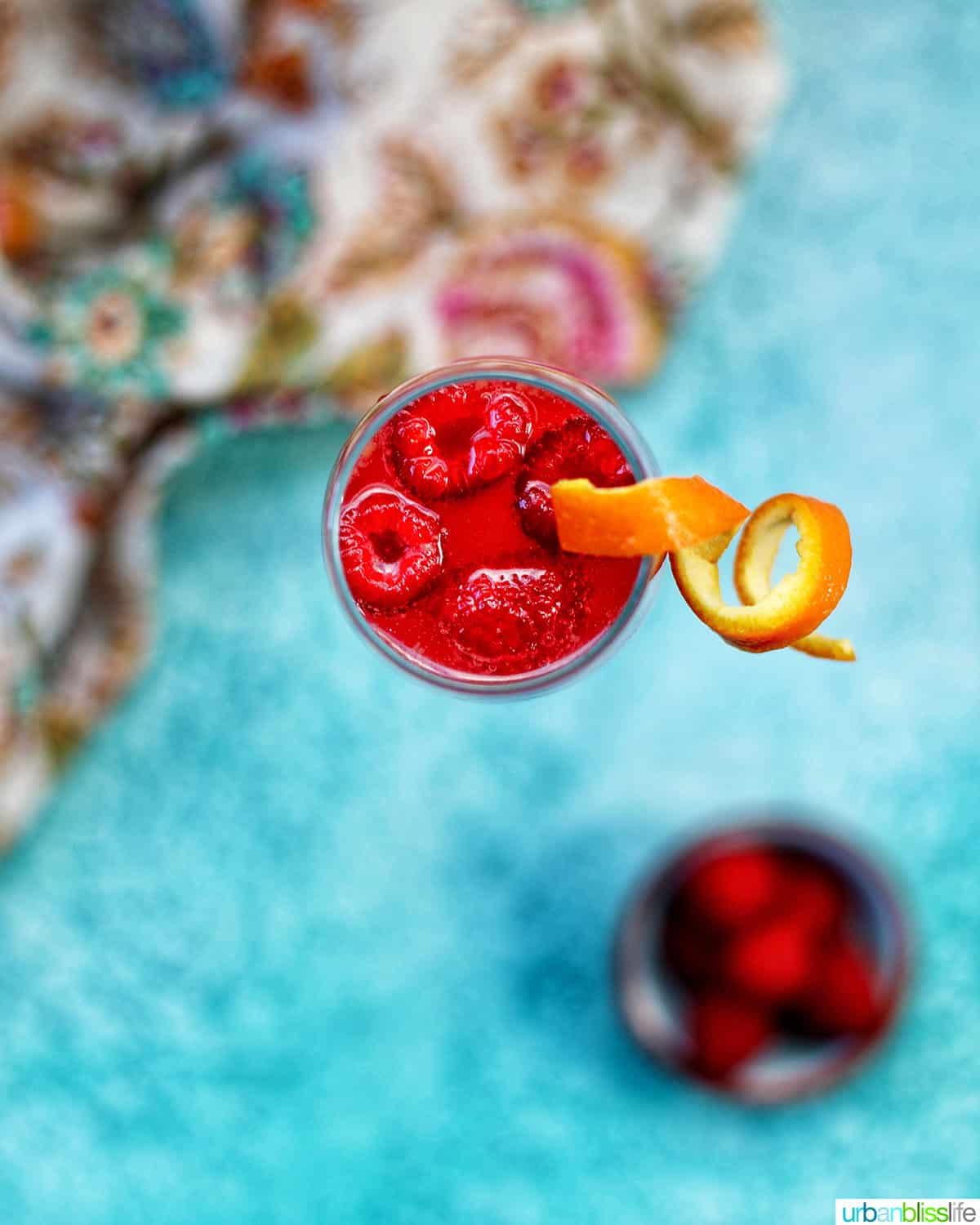 overhead photo of a Raspberry Mimosa with raspberries and orange rind garnish on blue background.