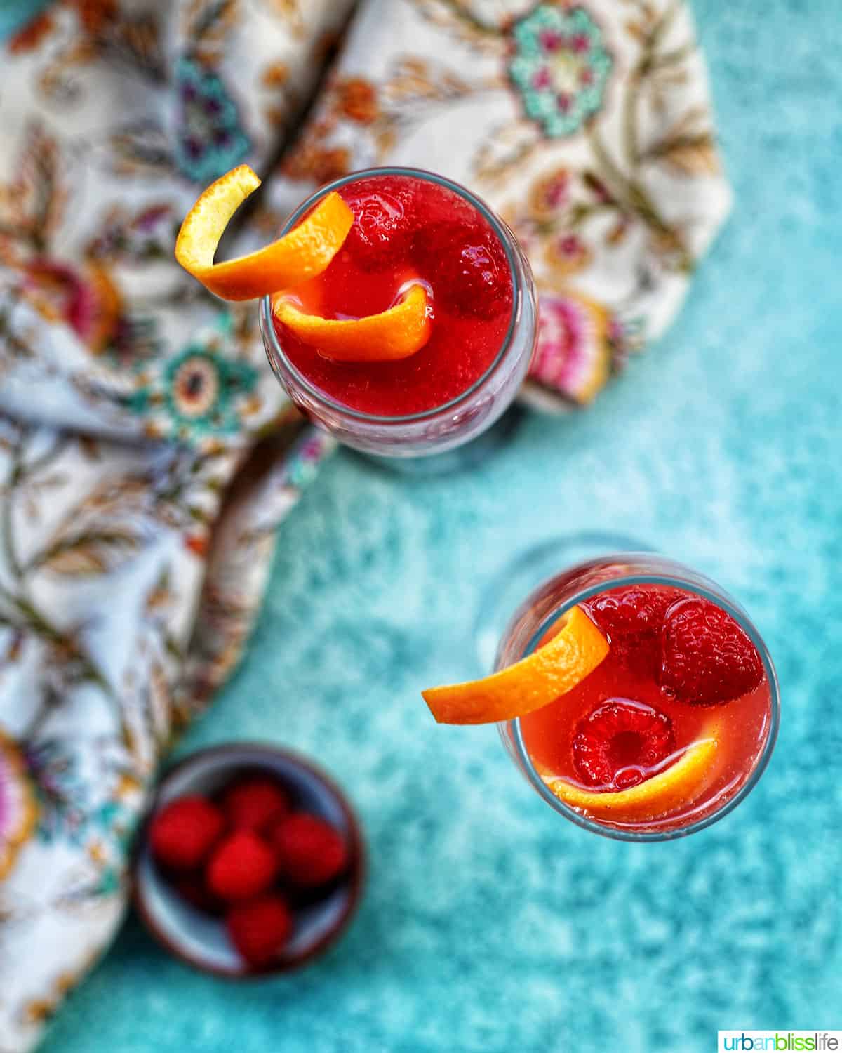 Raspberry Mimosa with raspberries and orange rind garnish on blue background.