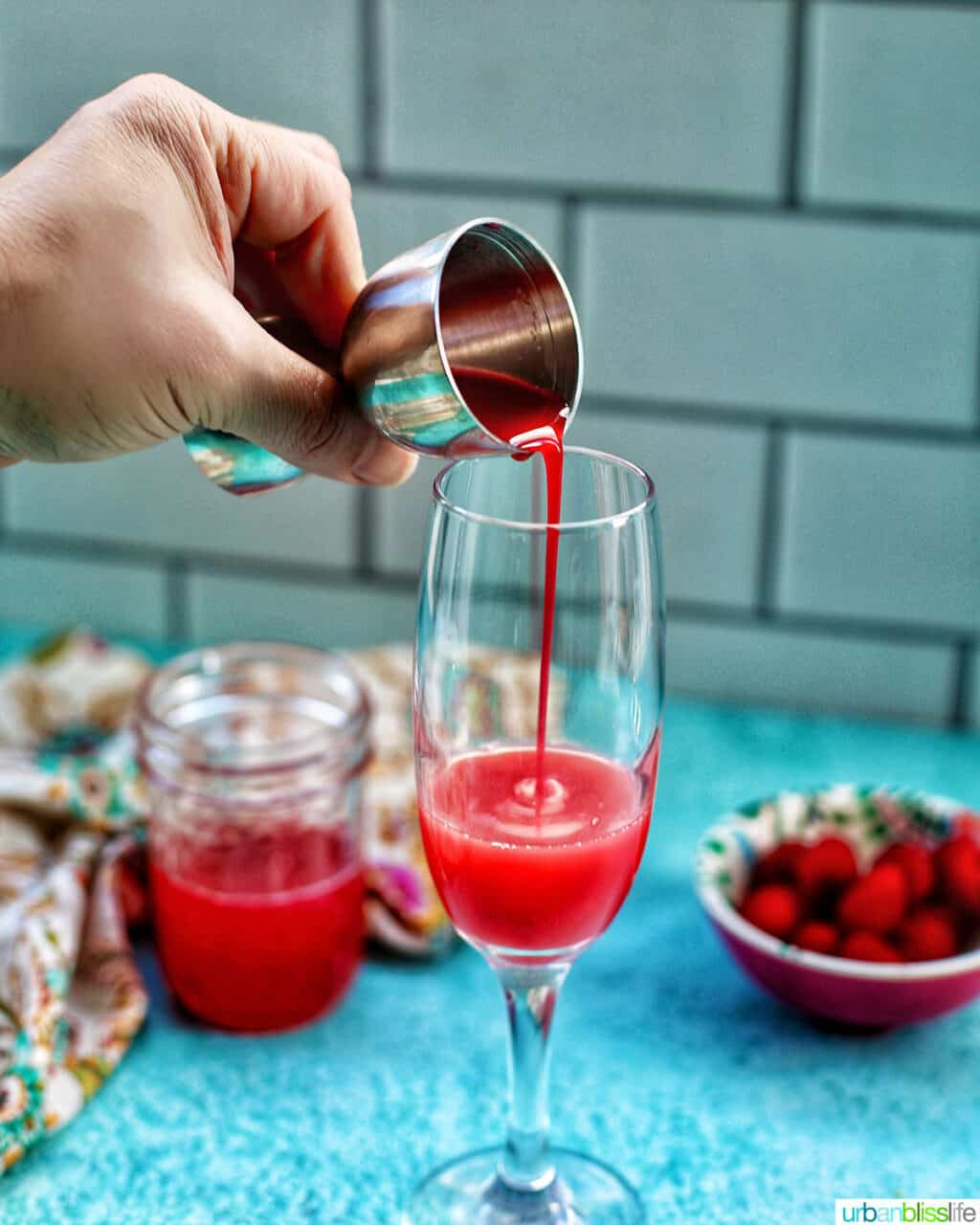 pouring raspberry puree into a glass to make Raspberry Mimosas