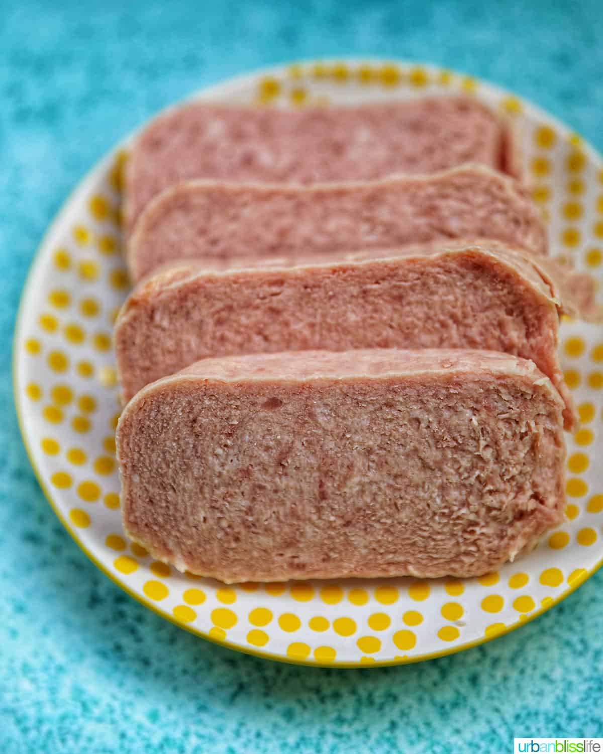 sliced spam on a white plate with yellow polka dots on a blue table.