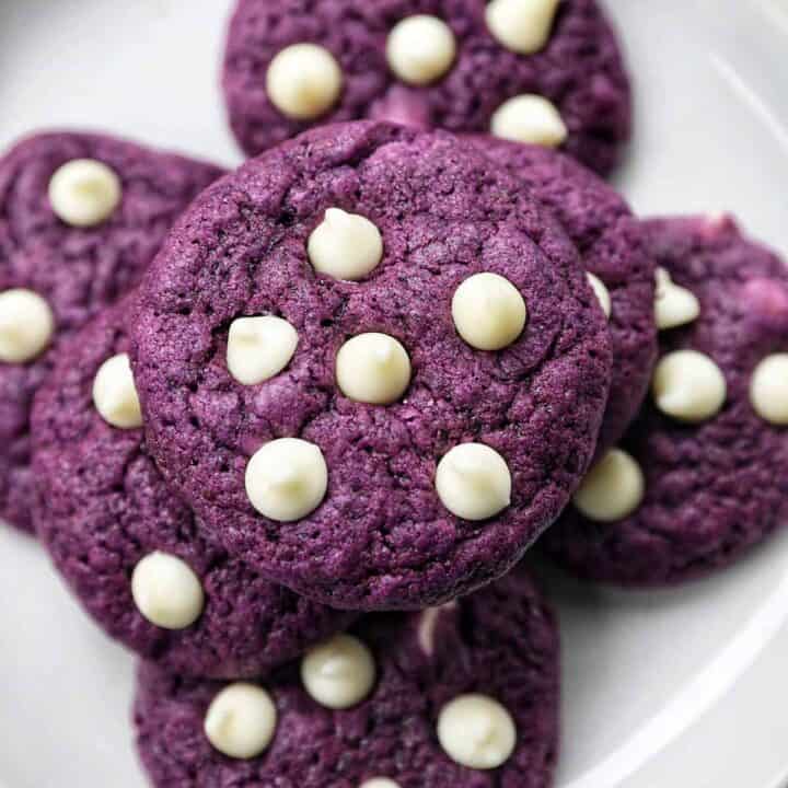 ube white chocolate chip cookies stacked on top of one another on a white plate.