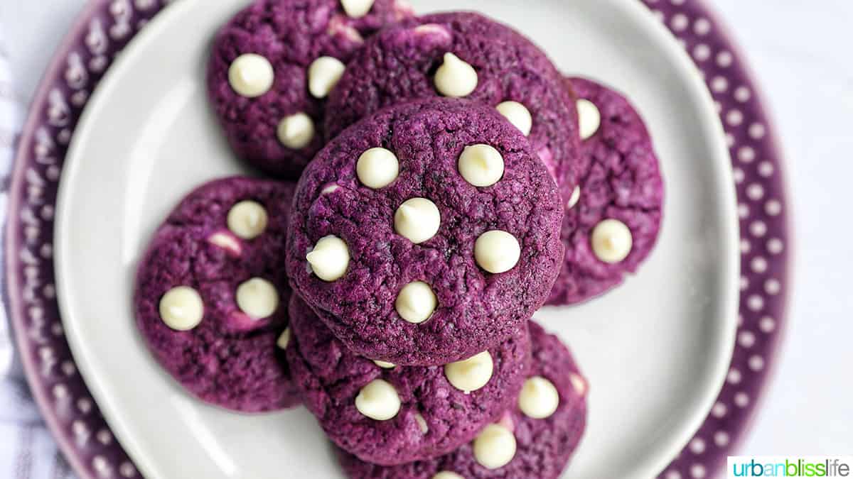 landscape photo of stacks of bright purple Ube cookies with white chocolate chips on a white and purple plate.