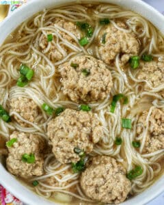 soup of meatballs and thin noodles in a white bowl.