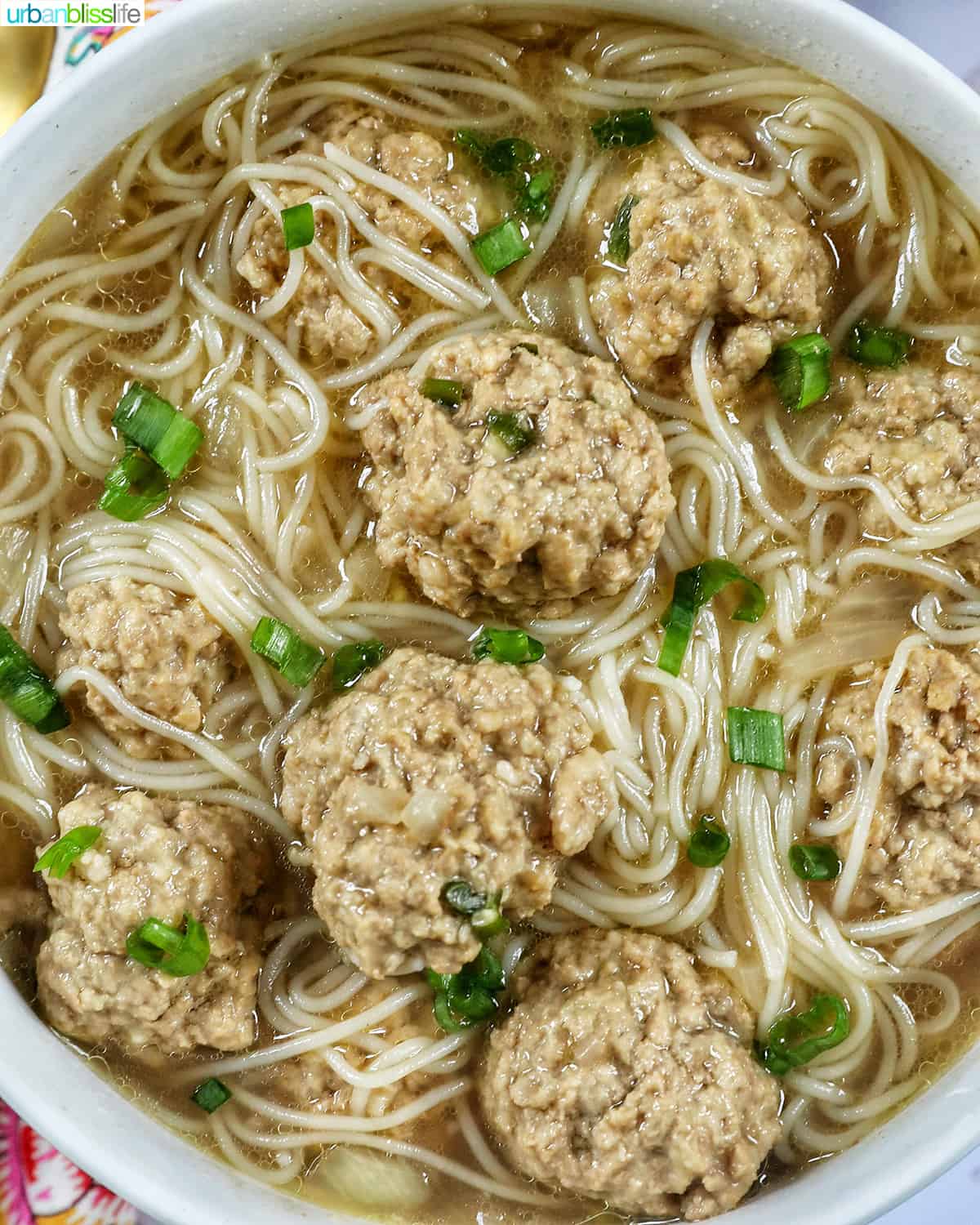 closeup of a bowl of filipino almondigas, meatball and thin noodle soup, with sliced green onions.