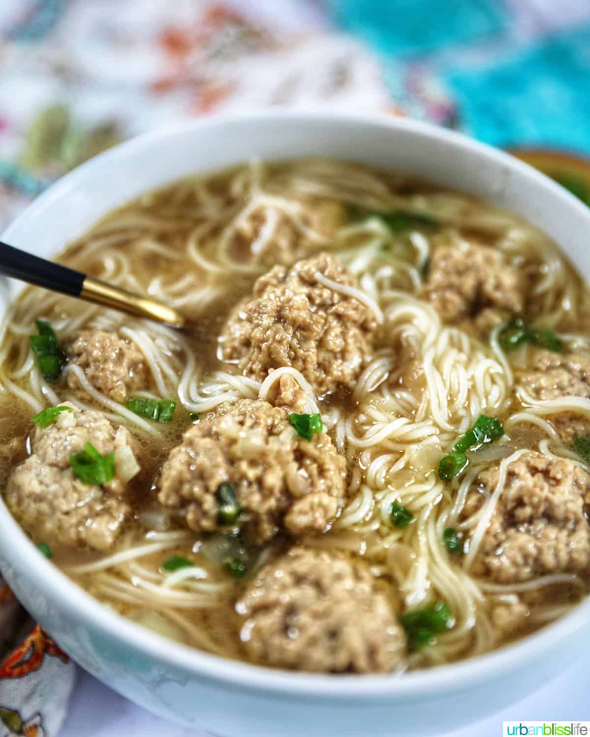 filipino almondigas meatball and thin rice noodle soup in a white bowl with a spoon.