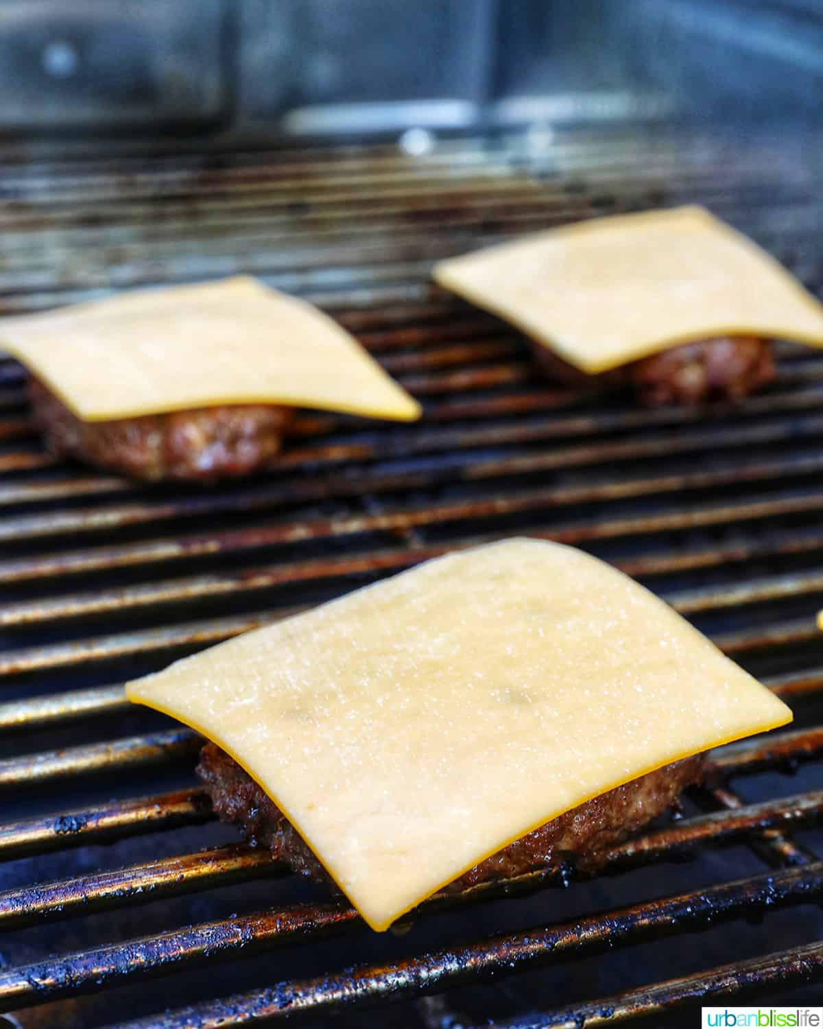 burgers topped with cheese on a grill