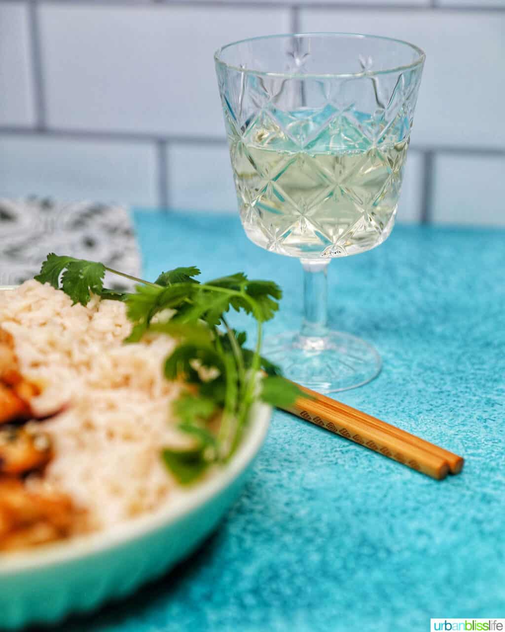 glass of white wine with rice and asian chicken dish