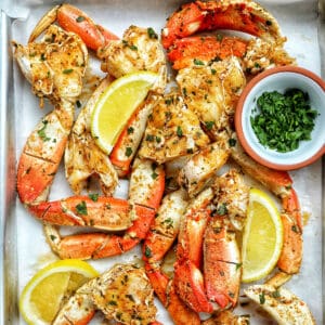 crab legs on a tray with lemon wedges and chopped parsley.